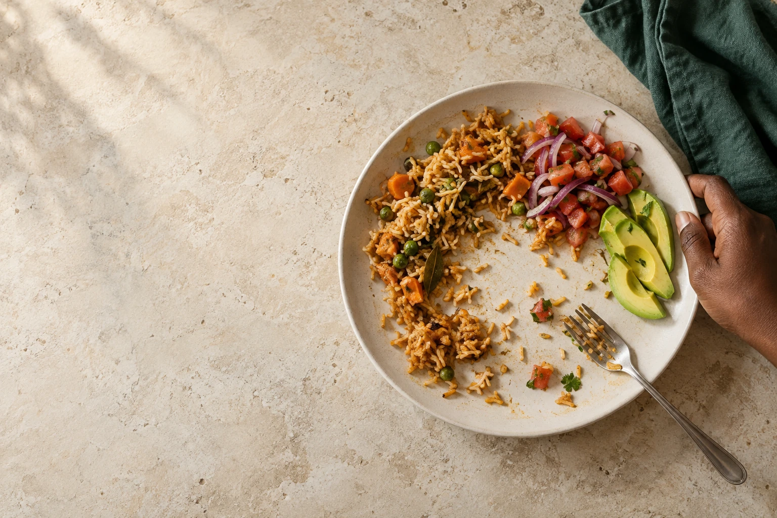 A hand clears a plate with pilau, kachumbari and avocado left uneaten
